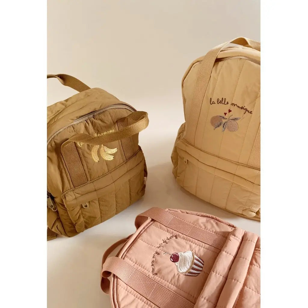 Beiger gesteppten, wasserfesten Kinder-Rucksack mit bestickter Banane und Text „la belle musique“, entworfen für den Schulgebrauch.