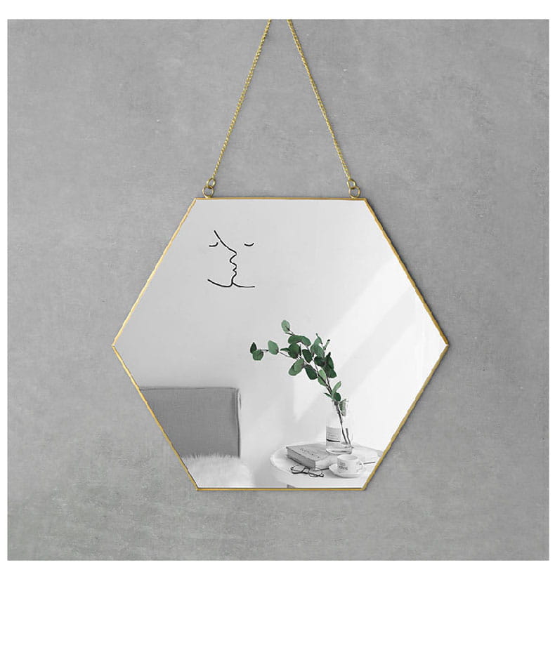 Gold hexagonal wall hanging mirror features a gold frame with a minimalist black line drawing of lips on the reflective surface, suspended by a matching gold chain.