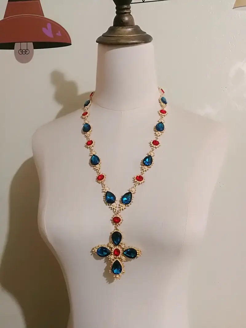 Collier ras du cou à déclaration en cristal à finition dorée, saisissant, avec un pendentif en forme de croix audacieux, orné de cristaux bleu profond en forme de larme et de cristaux ronds rouges, rehaussés de pierres claires plus petites, idéal pour des bijoux de soirée.