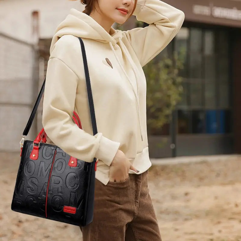 Black crossbody handbag in style1 style2 made of black pu leather with red accents and embossed lettering in satchel design.