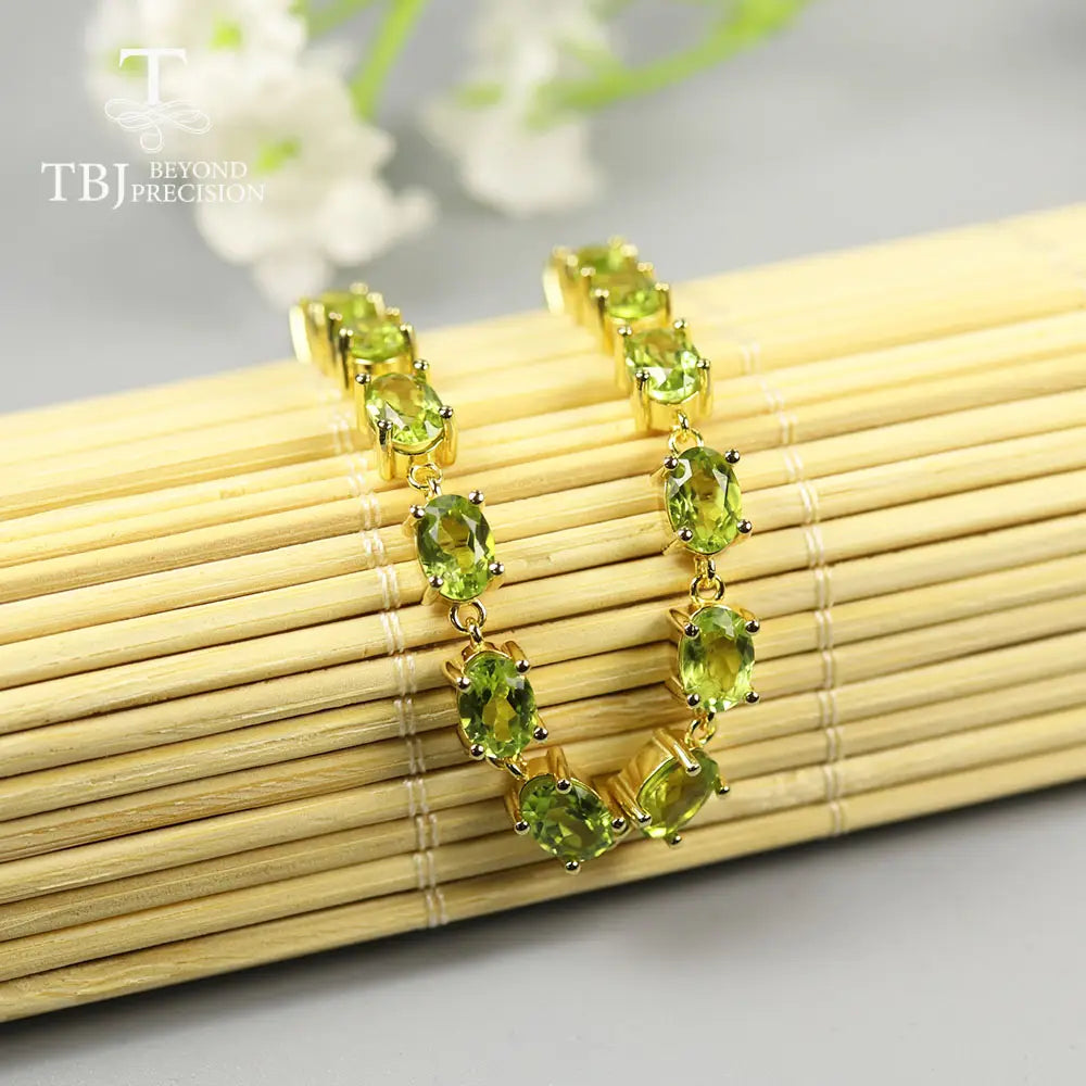 Una pulsera tipo tenis delicada de plata de ley con peridoto en tono dorado, con una fila de piedras ovaladas verdes de peridoto vibrantes colocadas en engastes.