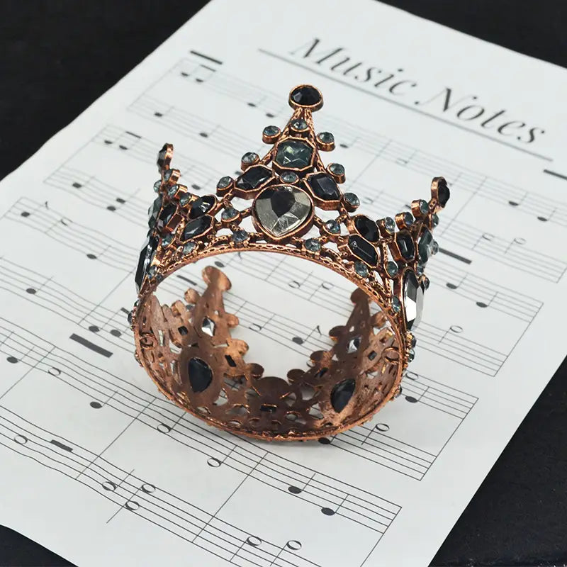Ein kunstvoller Mini-Kronen-Tortenaufsatz und eine Haar-Tiara aus Roségold, verziert mit dunkelblauen und klaren facettierten Edelsteinen.