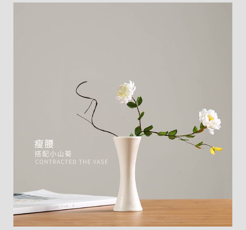 A modern white ceramic vase with a sleek off-white hourglass silhouette holds two delicate white flowers for floral decor.