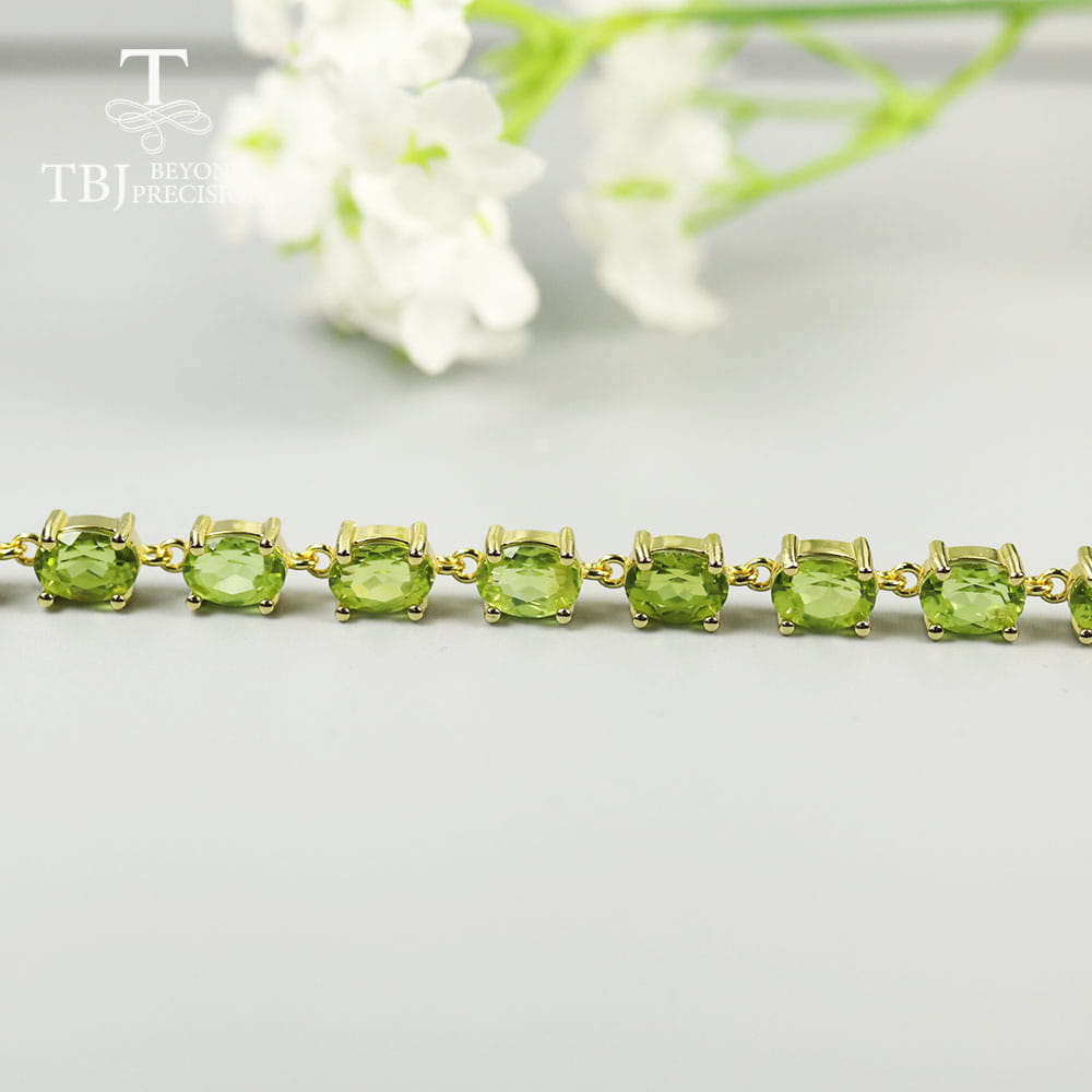 Una pulsera tipo tenis delicada de plata de ley con peridoto, con engastes en tono dorado y piedras ovaladas facetadas dispuestas de manera uniforme.