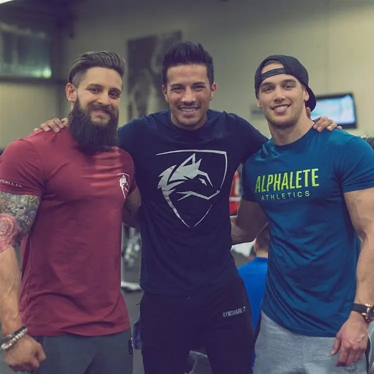 T-shirt d’entraînement en coton noir pour homme, avec logo de loup gothique, emblème de loup blanc et texte vert Alphalete Athletics, pour le streetwear.