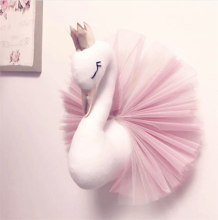 Eine plüschige weiße Schwan-3D-Cartoon-Tierkopf-Wanddekoration mit einem rosa Tüllrock und einer kleinen Krone.