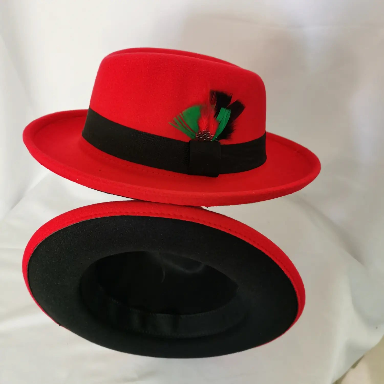 Unisex woolen felt fedora hat in vibrant red with a black band and green and black feather accent.