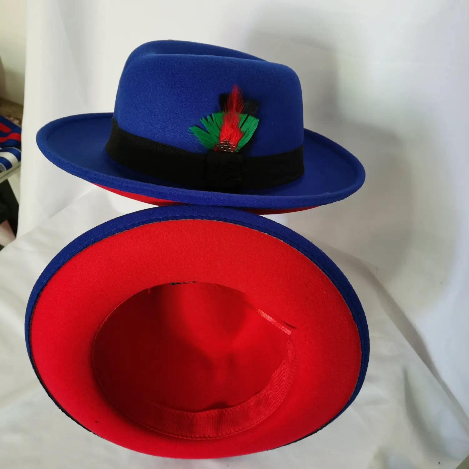 Vibrant blue unisex woolen felt fedora hat with a black band red interior and colorful feather accent.