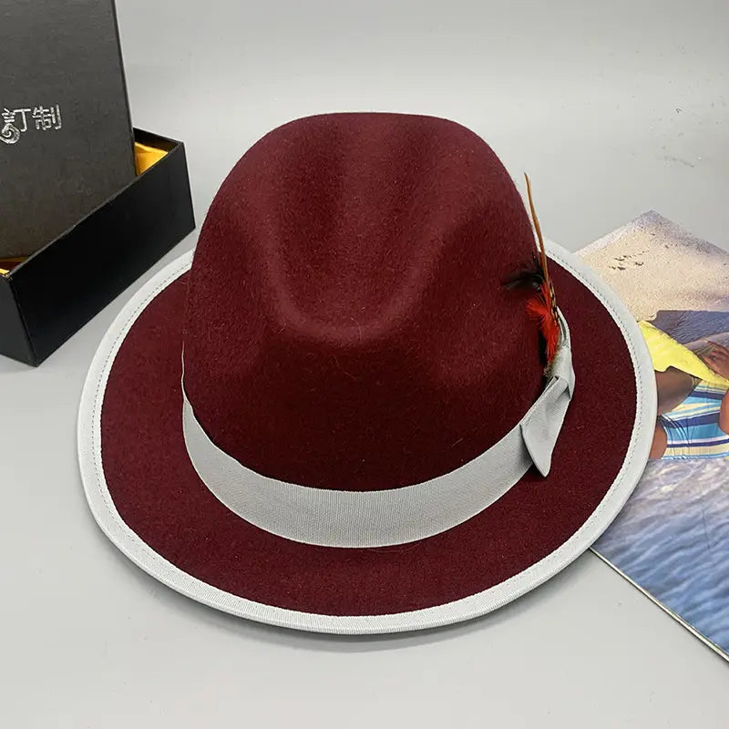 A unisex maroon woolen felt fedora hat with a white ribbon band and decorative feather accent.