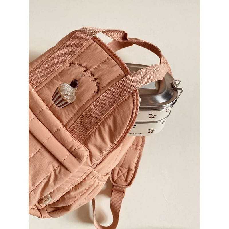 Ein weicher rosafarbener Kinder-gesteppten Rucksack aus wasserfestem Material mit einem bezaubernden bestickten Cupcake-Design auf der Vorderseite, geeignet für den Schulgebrauch.