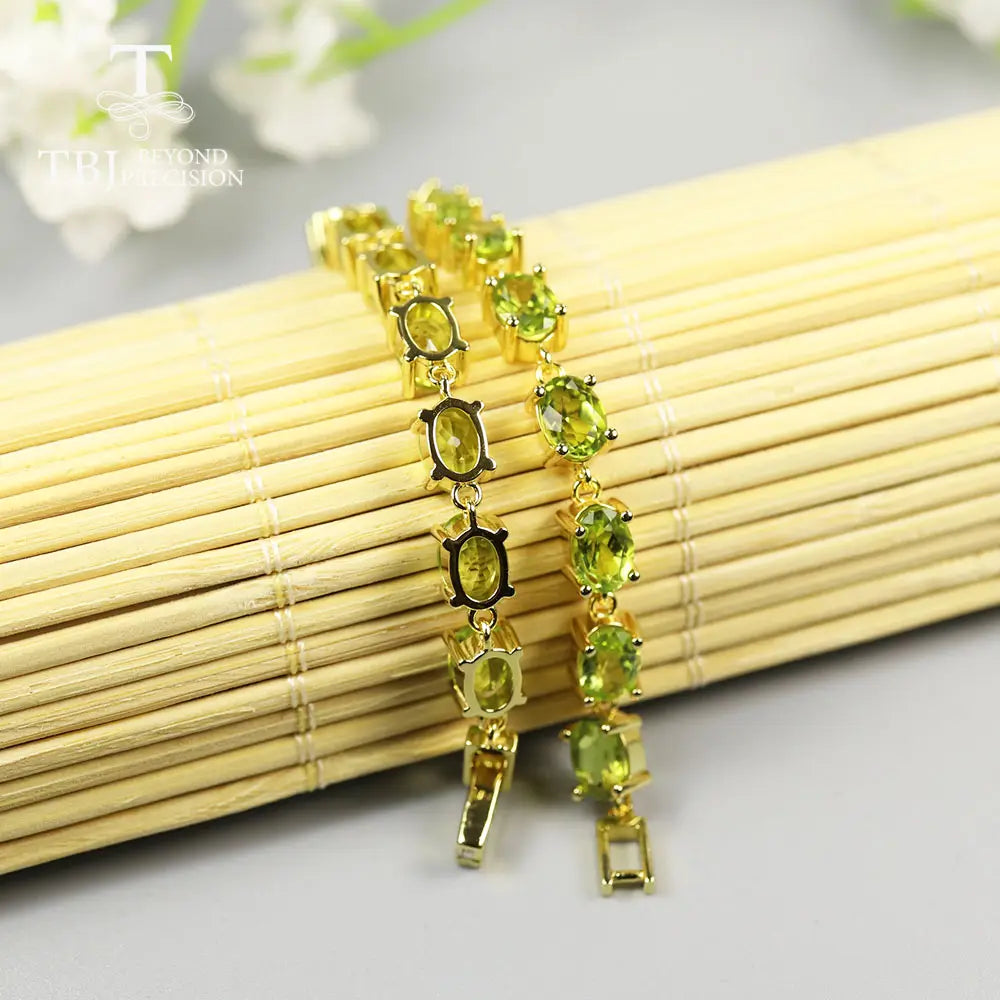 Un par de pulseras tipo tenis elegantes de plata de ley en tono dorado, con piedras ovaladas de peridoto colocadas en un diseño de eslabones delicados.