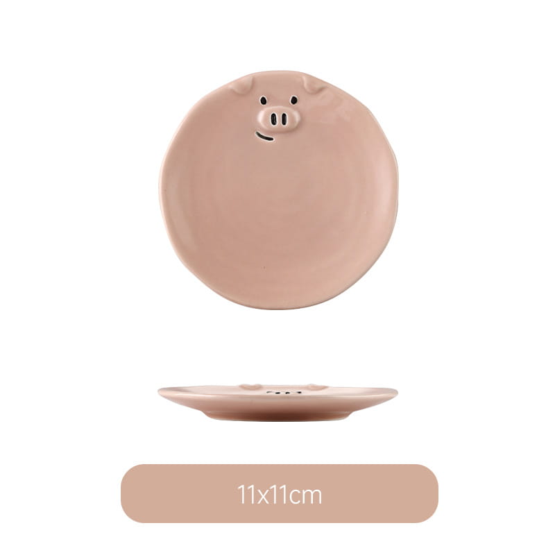 A blush pink ceramic plate shaped like a round pig with black dot eyes snout and smiling mouth from the cute pig ceramic dinnerware set.