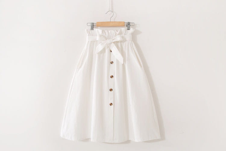Une jupe midi en coton blanche avec taille haute, ceinture froncée, nœud en tissu assorti et cinq boutons ton or sur le devant, conçue comme une robe décontractée en ligne A.