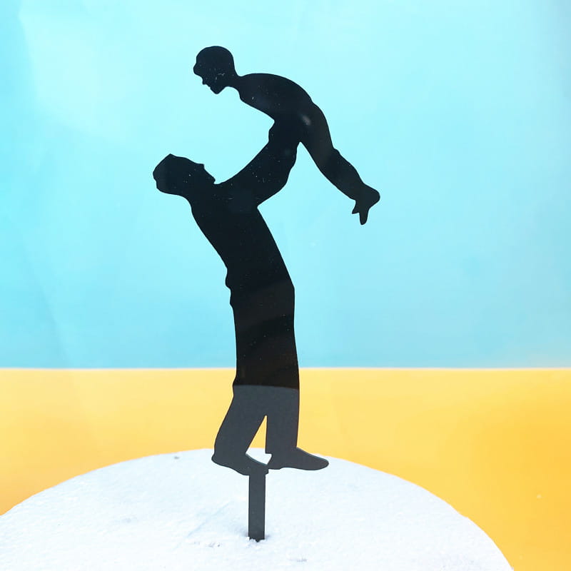 Black metal silhouette acrylic cake topper depicting a man lifting a child designed for Father’s Day super dad celebration.