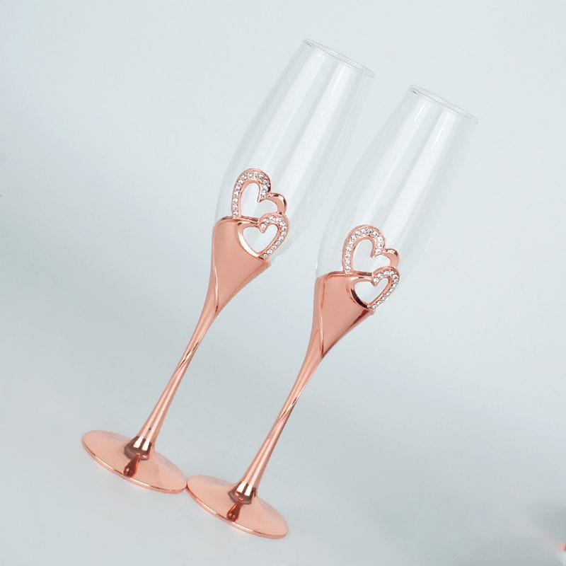 A pair of rose gold wedding champagne flutes with heart-shaped rhinestone embellishments ideal for toasting.