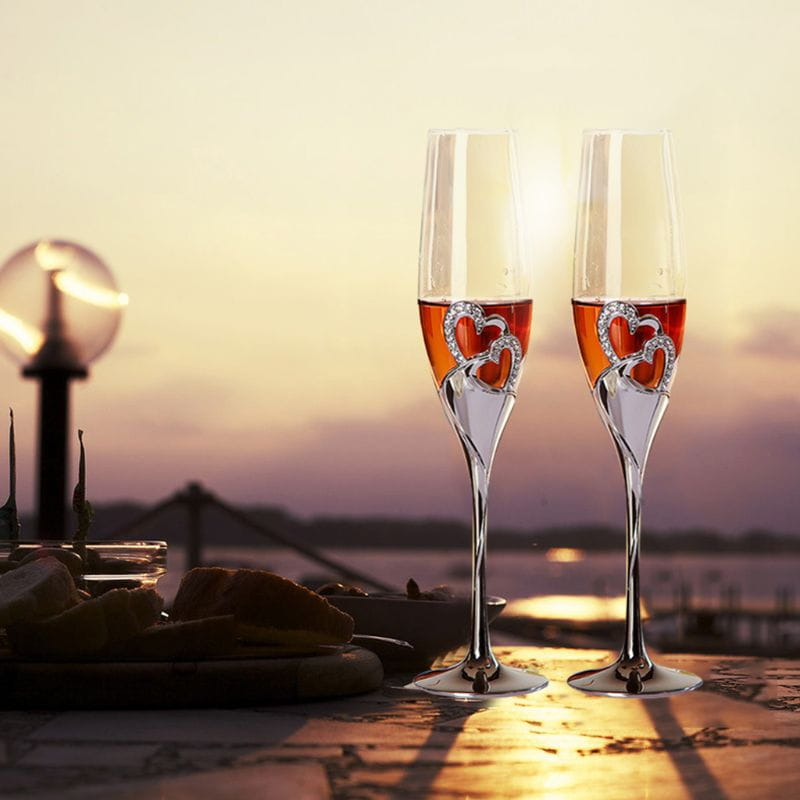 Two elegant crystal wedding champagne flutes with gold heart-shaped embellishments near the base for toasting.