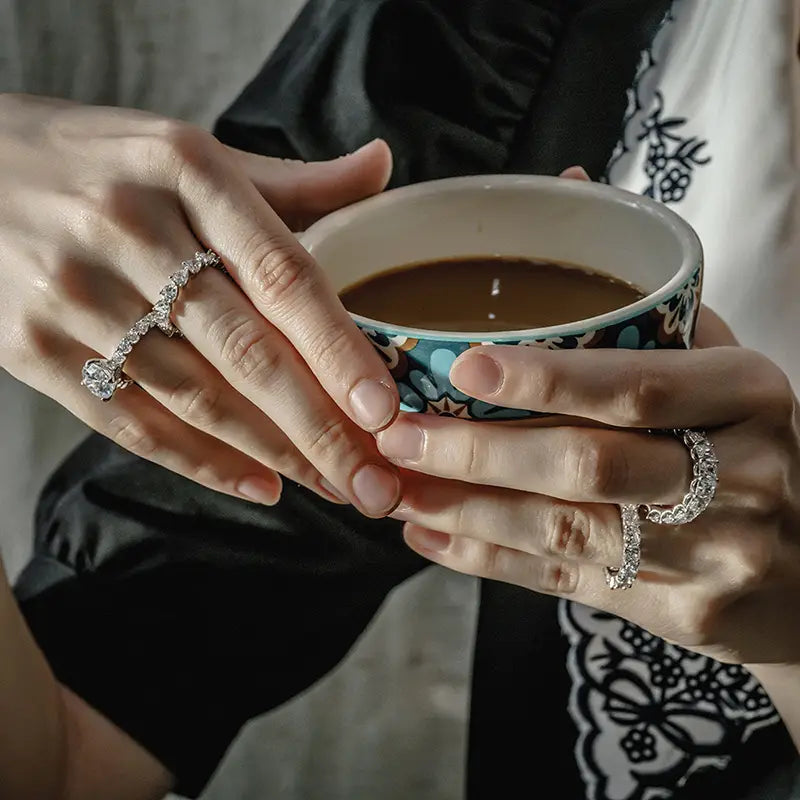 une bague d’éternité cœur en argent sterling présentée à côté d’une tasse en céramique avec un motif floral bleu et blanc, remplie de café noir