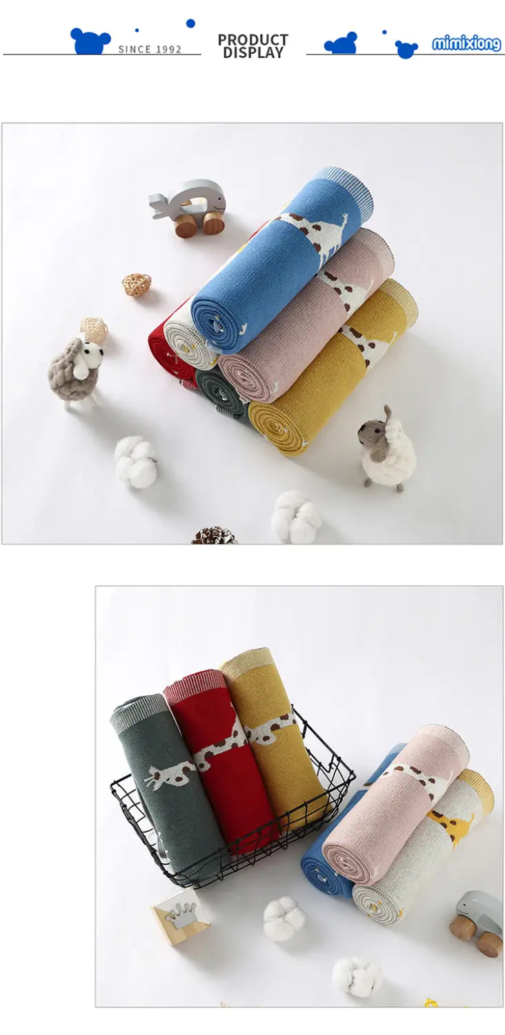 Aufgerollte gestrickte Baumwoll-Babytdecke mit Giraffen mit bezaubernden Kuhmustern mit weißen Punkten auf weichen Pastell- und kräftigen einfarbigen Untergründen.