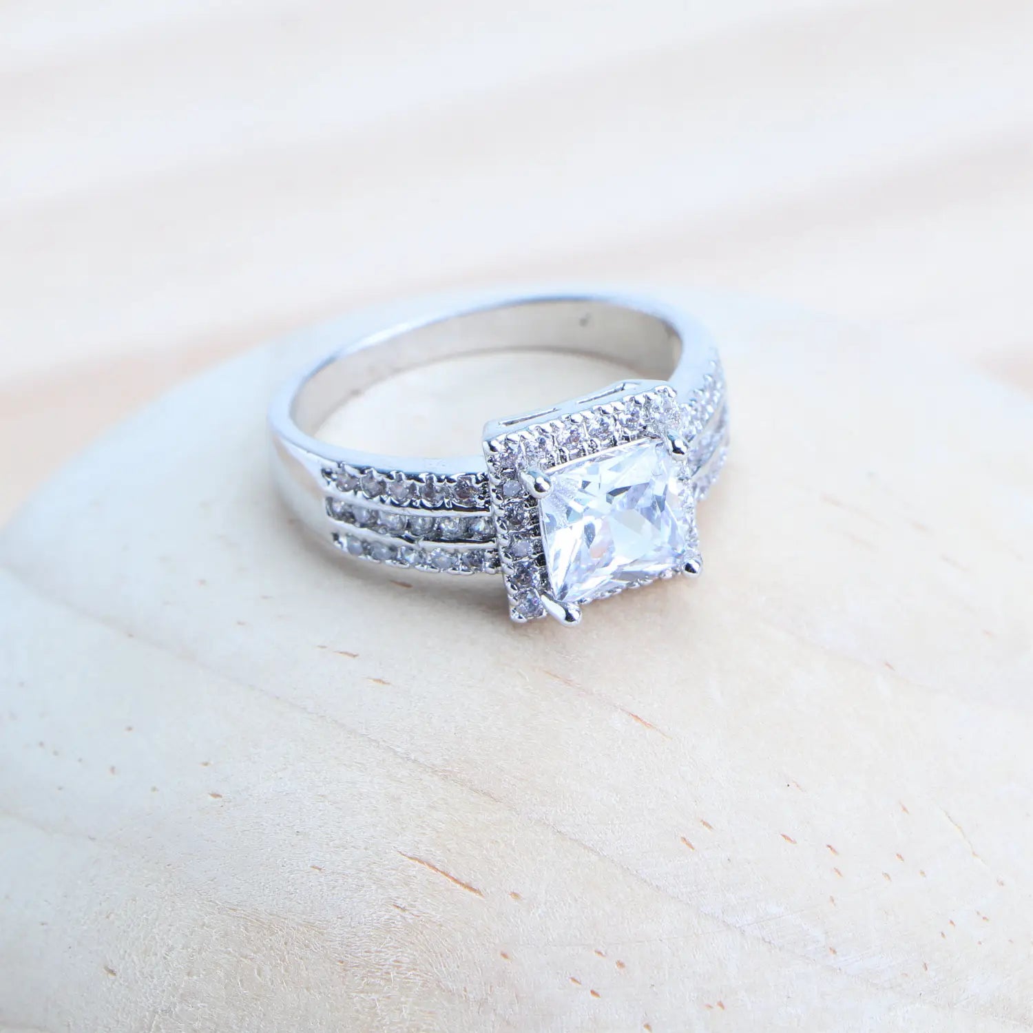 Un anillo nupcial de plata de ley 925 con tono plateado, que presenta una destacada gema de cristal transparente de talla cuadrada rodeada de piedras pequeñas engastadas tipo pavé, con filas adicionales de diminutos diamantes a lo largo de la banda.