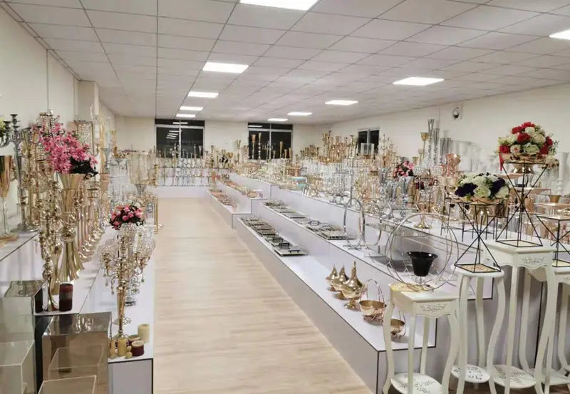 Rangées de chandeliers ornés dorés et argentés avec des compositions florales complétant un support de fond d’arche de mariage dorée pour des réceptions.