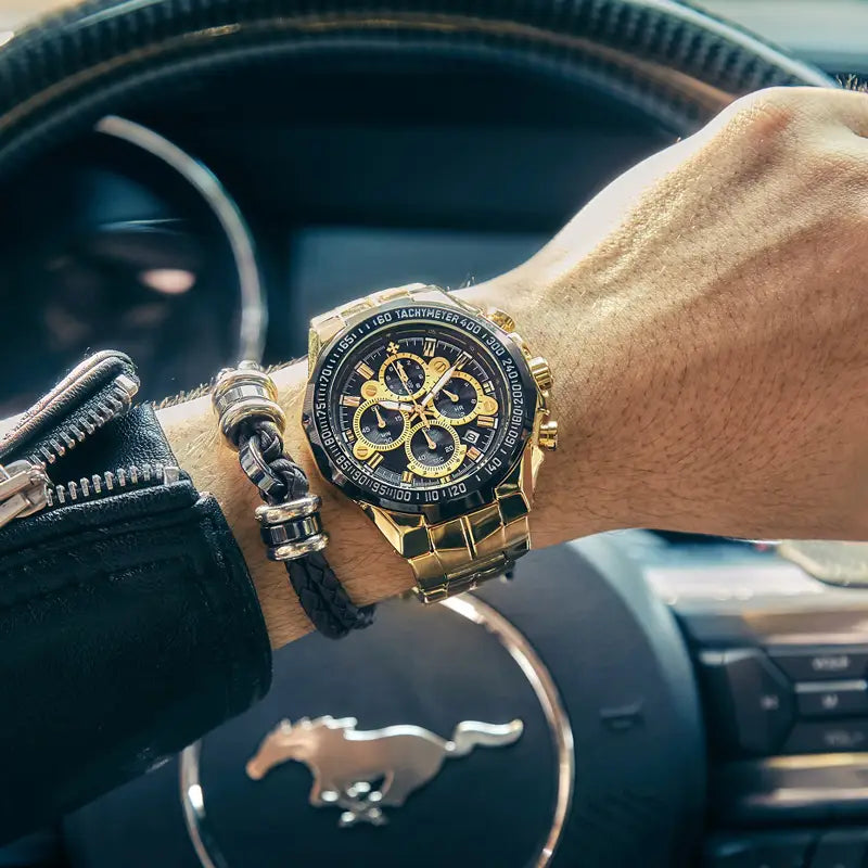 Gold chronograph watch men stainless steel luxury timepiece with a gold-toned case, black dial, gold accents, multiple subdials, and a tachymeter scale on the bezel.