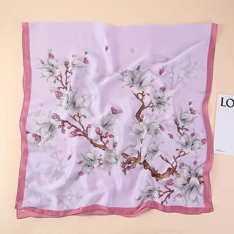 Un châle foulard en soie lilas délicat, présentant un imprimé aquarelle doux de branches de cerisiers en fleurs avec des boutons roses et des fleurs blanches, encadré par une bordure assortie en satin rose, inspiré par les amandiers en fleurs de Van Gogh.