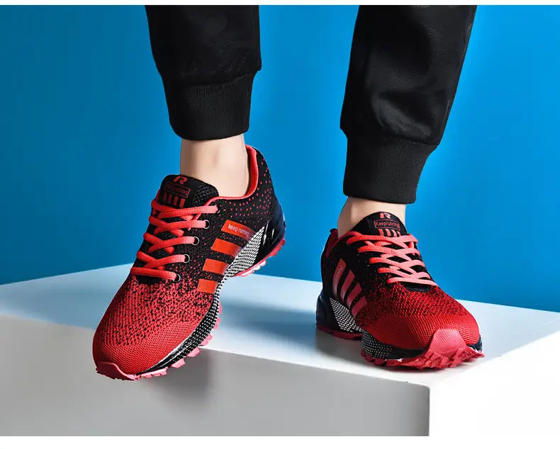 Chaussures de running pour hommes Covadis en maille respirante en rouge et noir, avec un dessus en maille respirante, des lacets rouges audacieux et trois bandes orange sur le côté.