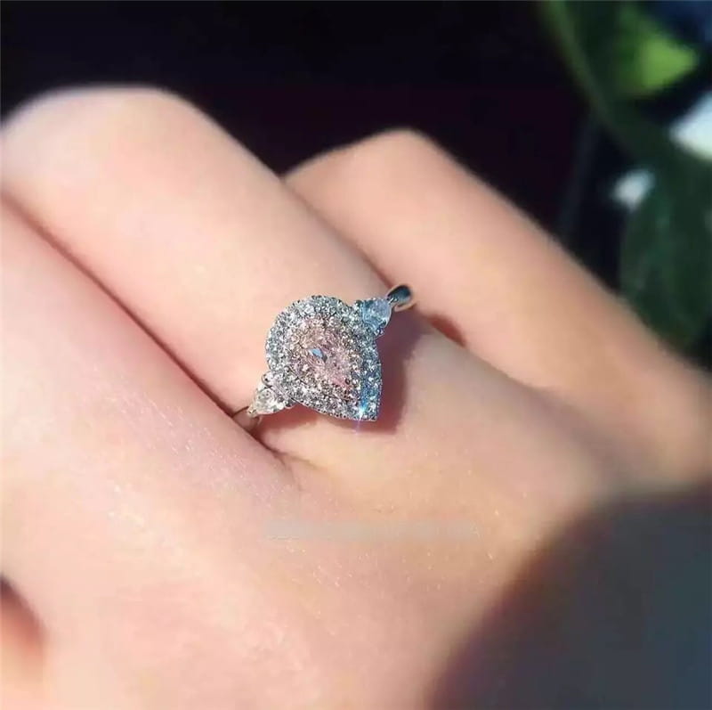 Bague de fiançailles en zircon goutte de larme rose, avec un centre étincelant serti dans une bande argentée élégante, dotée de détails pavés complexes.