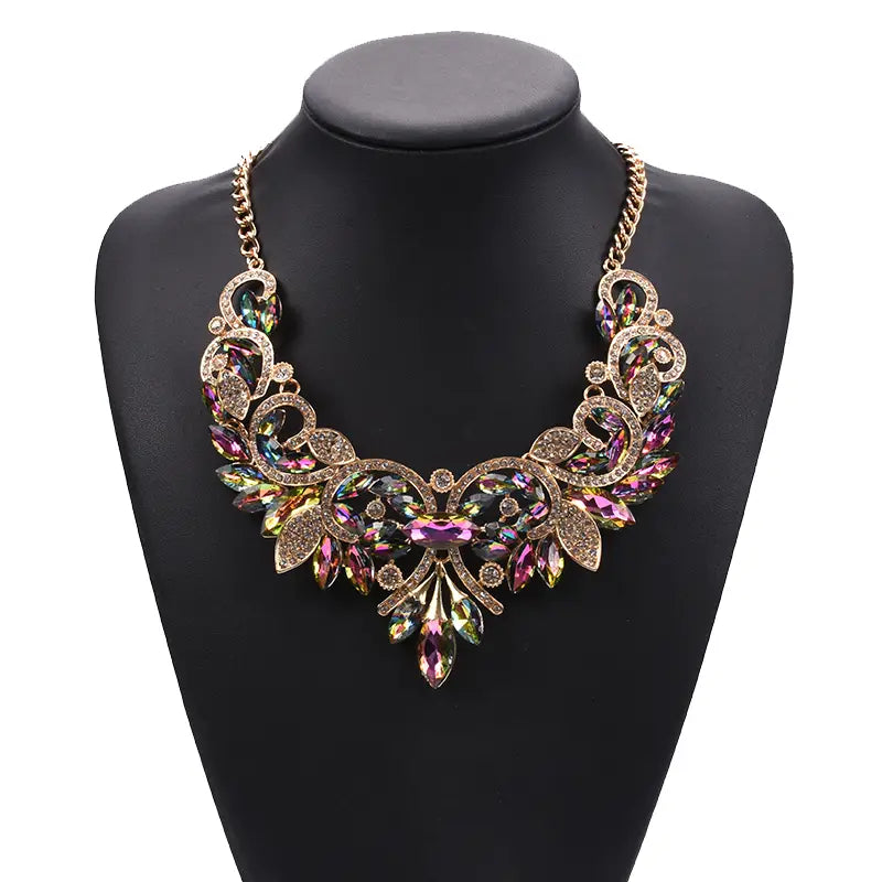 Un collier-sautoir en cristal aux tons dorés étincelant, présentant des motifs floraux et de feuilles complexes, rehaussés de cristaux irisés violet, vert et rose, dans un style bohème multicolore de ras-du-cou.