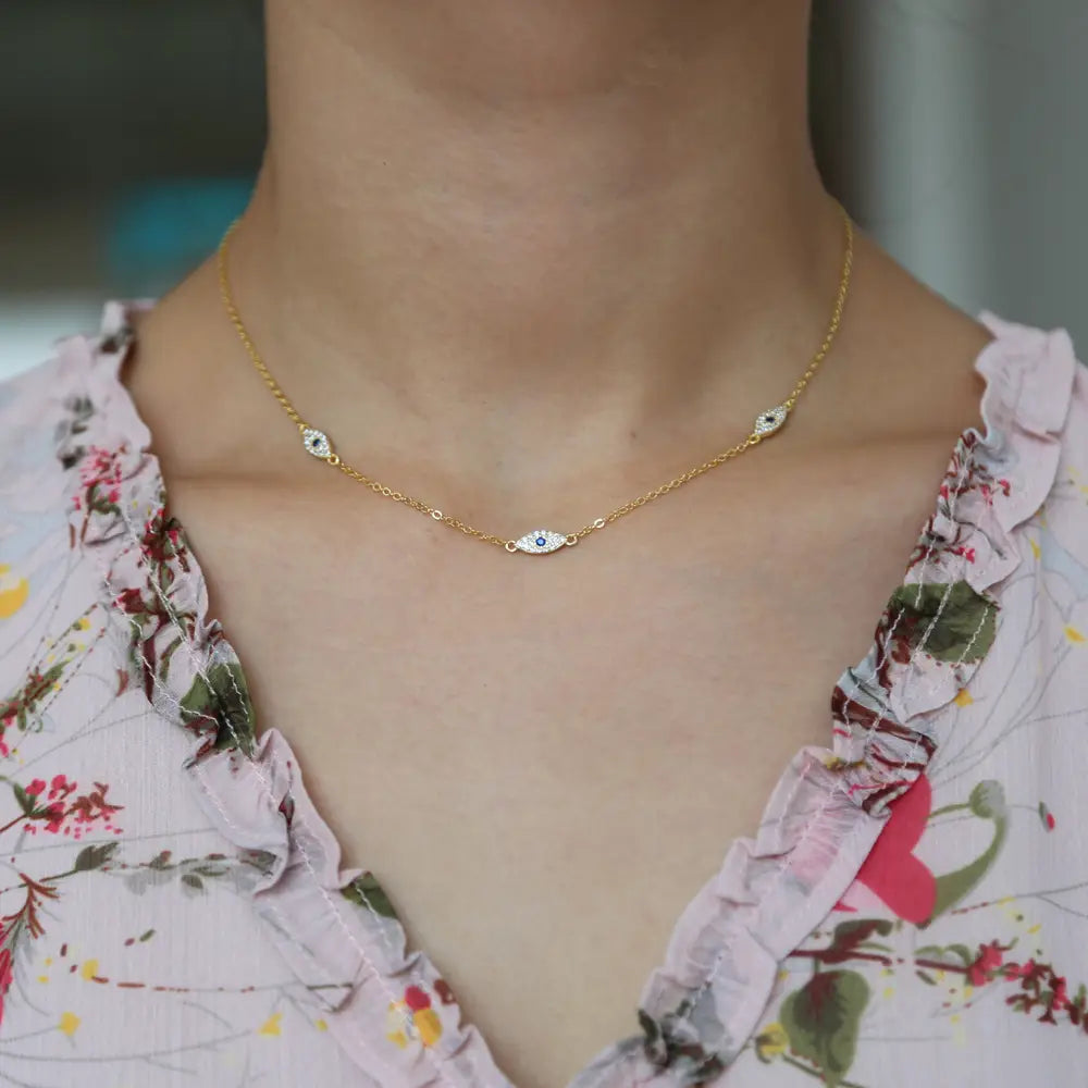 A delicate gold chain silver evil eye charm necklace featuring three small eye-shaped pendants with blue and clear cz crystal gemstones.