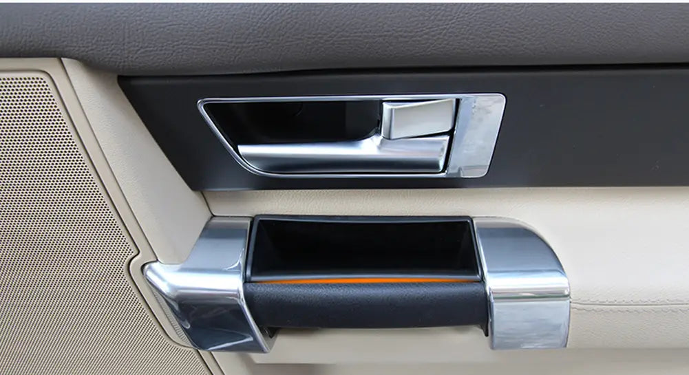 Le parement chromé de la boîte-plateau de rangement de poignée de porte pour Land Rover Discovery 4, avec poignée en cuir noir et bande d’accent orange, est présenté depuis l’arrière.