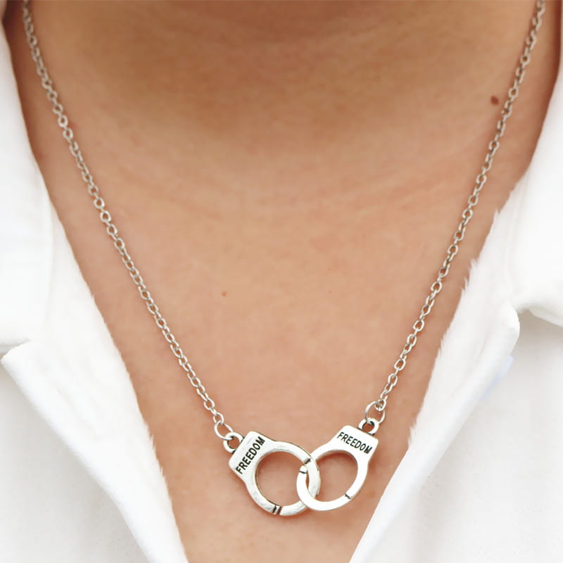 Silver-toned fashion jewelry necklace featuring interlocking handcuff pendants engraved with the word freedom.