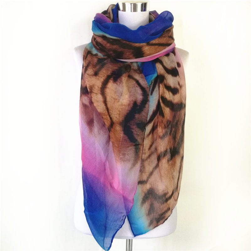Una bufanda-capa de visón con flecos de leopardo vibrante, que presenta un tejido translúcido con un estampado de tigre audaz y degradados en tonos marrón, negro, rosa y azul.