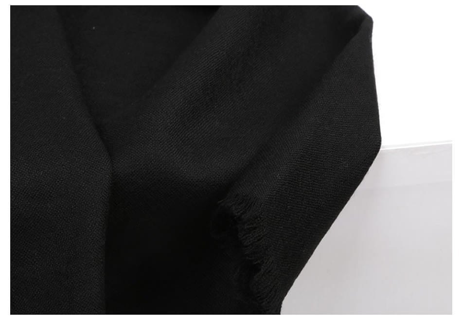Bufanda de lana de lujo para mujer en tela negra, con tejido suave ligeramente texturizado y bordes deshilachados.