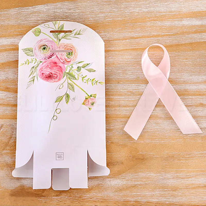 Sac cadeau en papier blanc avec design floral rose et vert, comprenant une ouverture de poignée découpée et un bord inférieur festonné, pour un lot de boîtes de faveur de mariage en papier floral rose de 50.