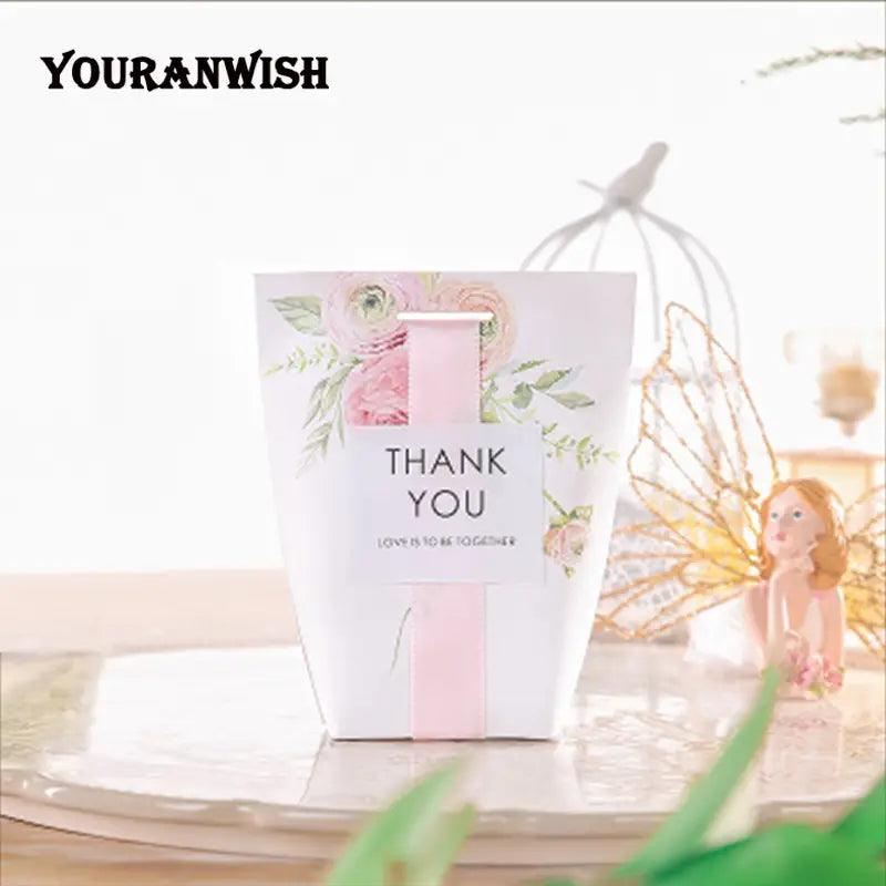 Sac cadeau délicat en papier blanc avec illustrations florales rose tendre et ruban rose assorti, comprenant un texte « merci » pour un lot de boîtes de faveur de mariage en papier floral rose de 50