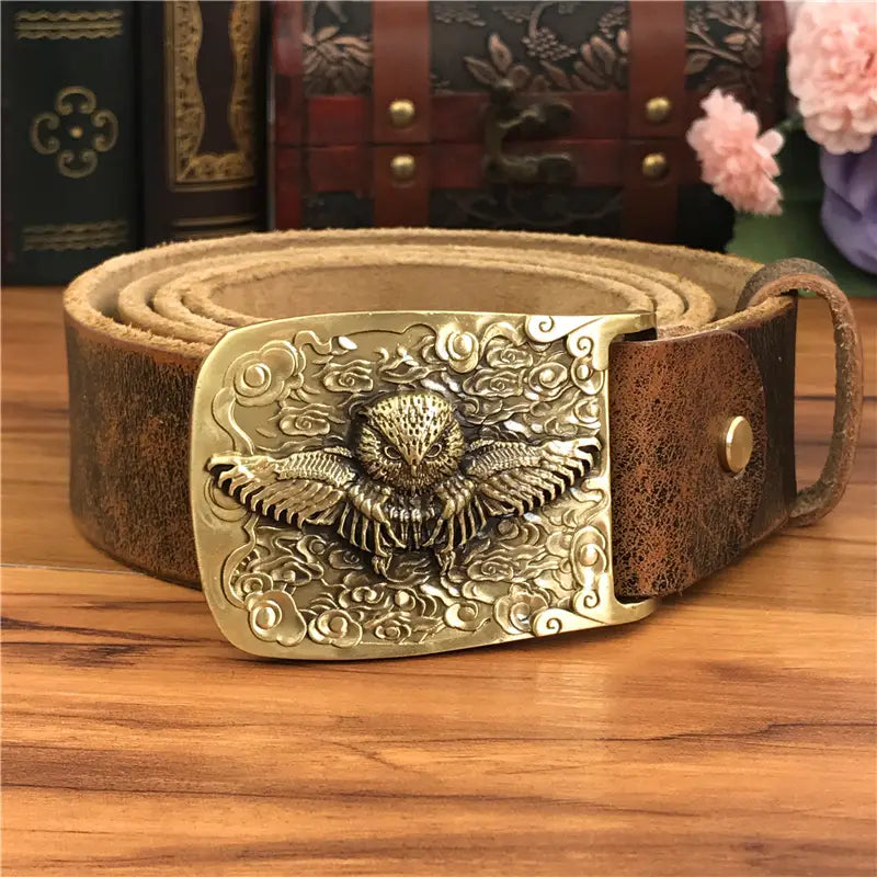 A vintage-style brown genuine leather men jeans belt featuring an intricately engraved brass owl buckle with detailed swirling cloud patterns.
