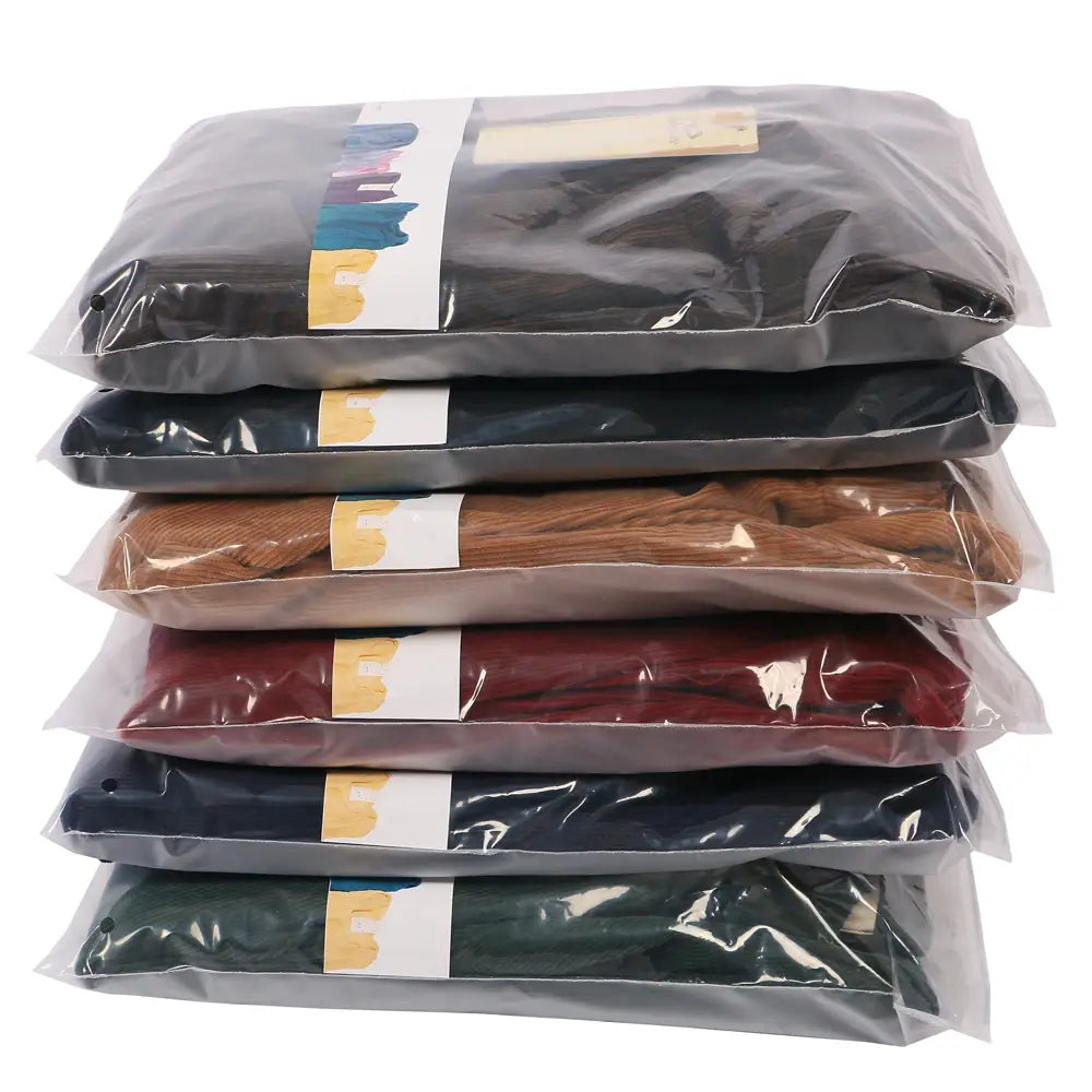 un conjunto de seis camisetas de color sólido surtido, empaquetadas individualmente en plástico transparente con etiquetas blancas que presentan acentos amarillos y multicolores, mostradas junto a pantalones de pana de pierna ancha con cintura elástica y ajuste holgado, que resaltan la longitud del pantalón en imágenes detalladas