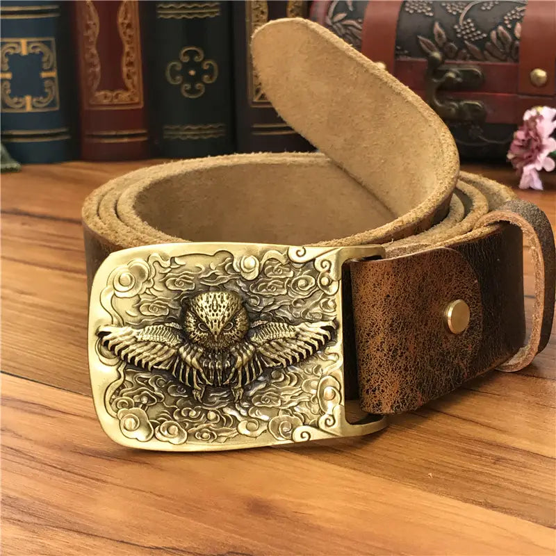 A bronze-colored brass owl belt buckle with intricate engravings on a dark brown genuine leather men jeans belt.