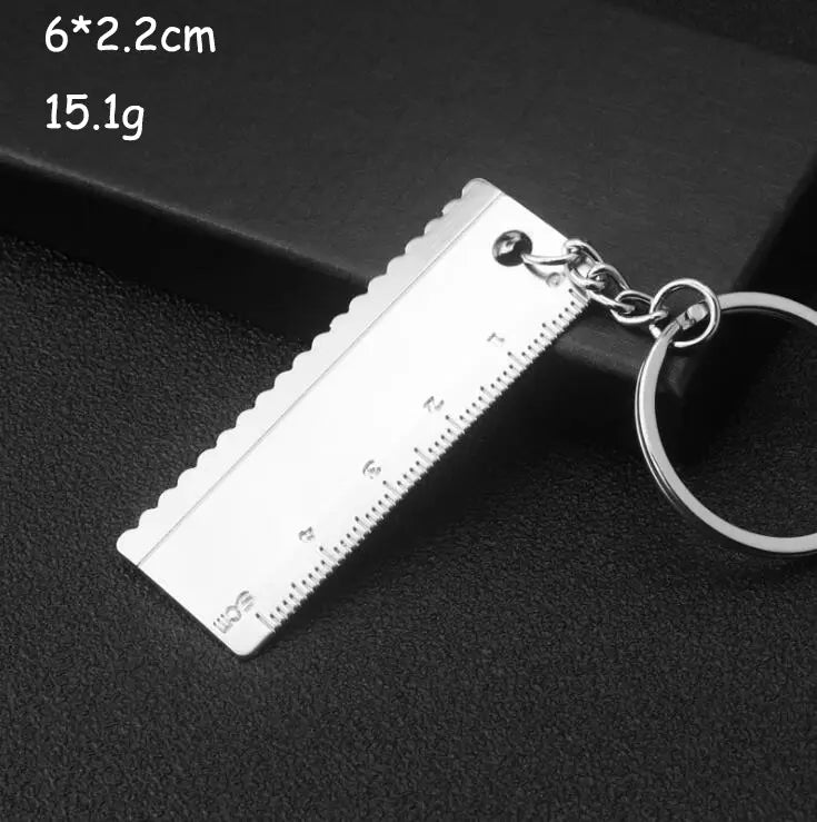 Silver metallic mini tool keychain shaped like a miniature ruler with serrated edges and engraved measurement markings for metal multi-tool key ring.