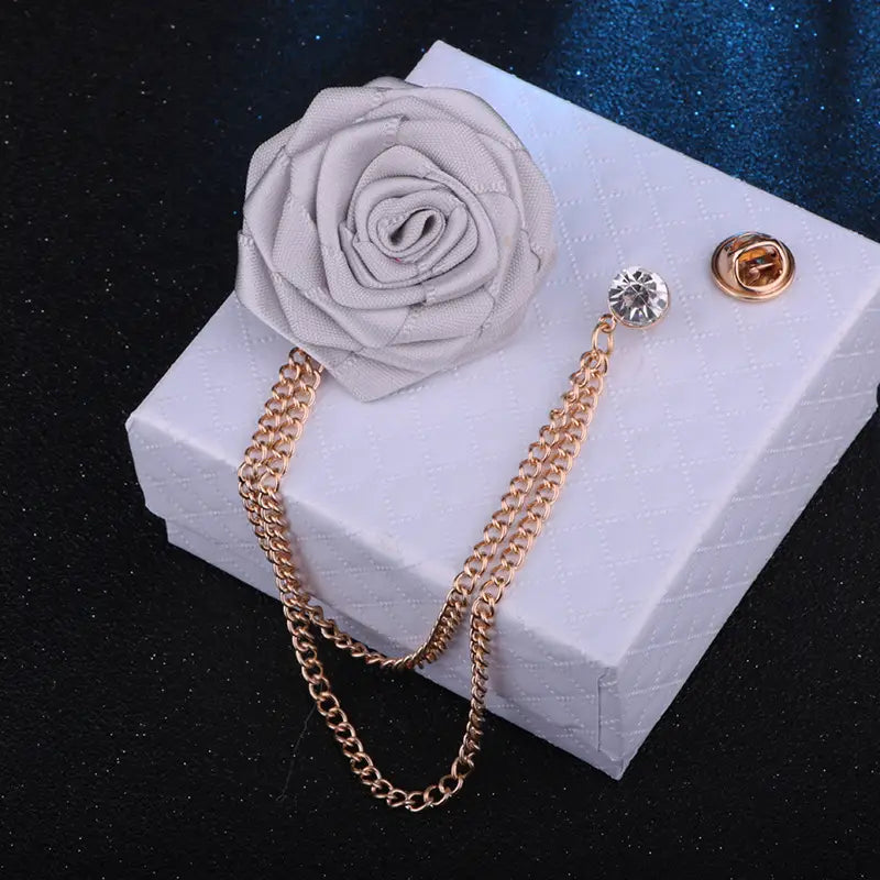 A delicate gray fabric rose brooch with a gold-toned tassel chain and crystal accent designed as a men suit pin.