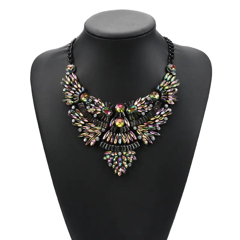 Un collier audacieux à chaîne noire, orné de rhinestones irisés multicolores disposés dans un motif complexe évoquant une plume, avec un design bohème multicolore.