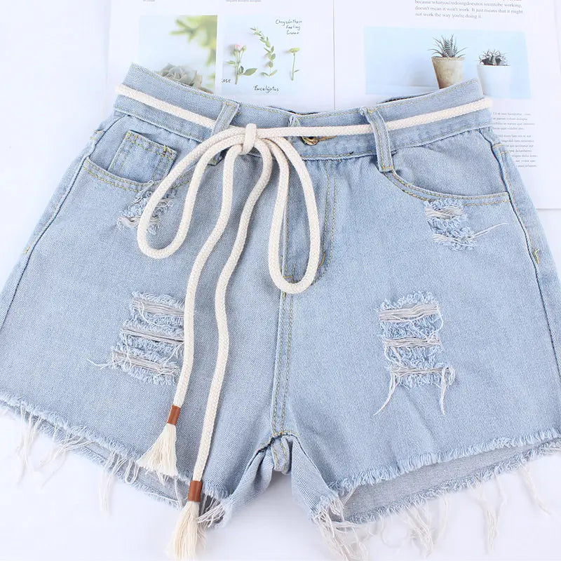 Light-wash denim shorts with distressed frayed details paired with a cream-colored braided rope belt women tassel waistband dress accessory.