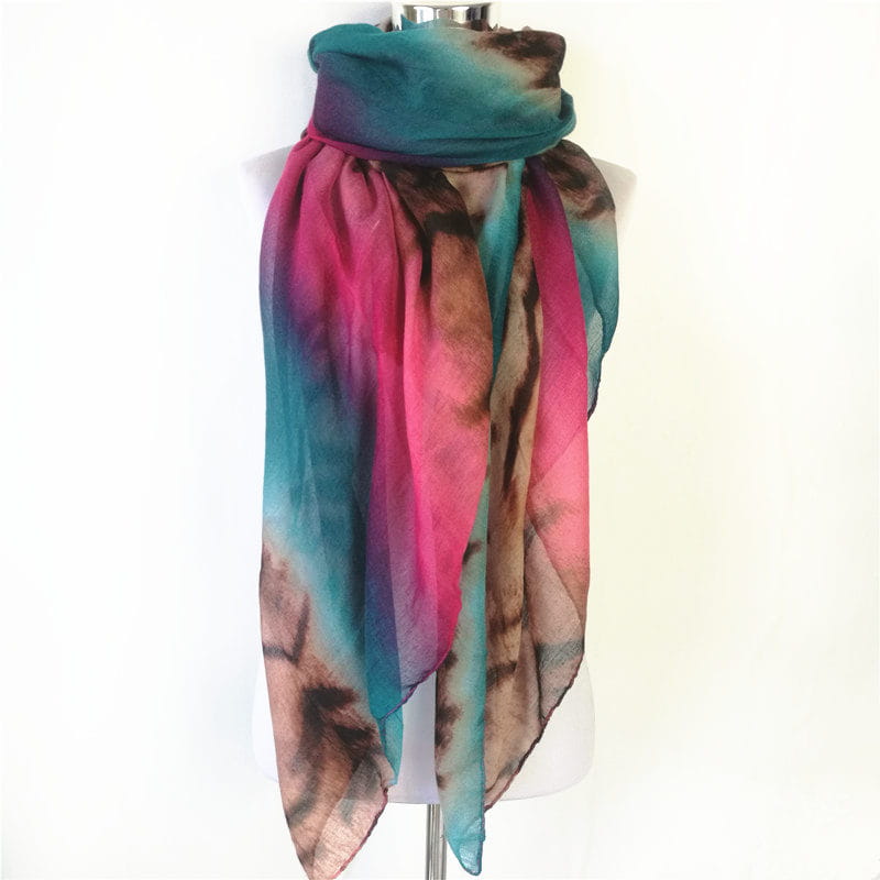 Una bufanda-capa de visón con flecos de leopardo con teñido anudado vibrante en tonos de verde azulado, rosa y marrón, drapeada con elegancia sobre un maniquí.