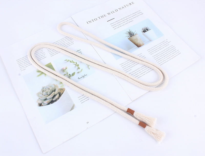 Cream-colored macrame cord braided rope belt with tassels and brown leather accents used as a women tassel waistband dress accessory.