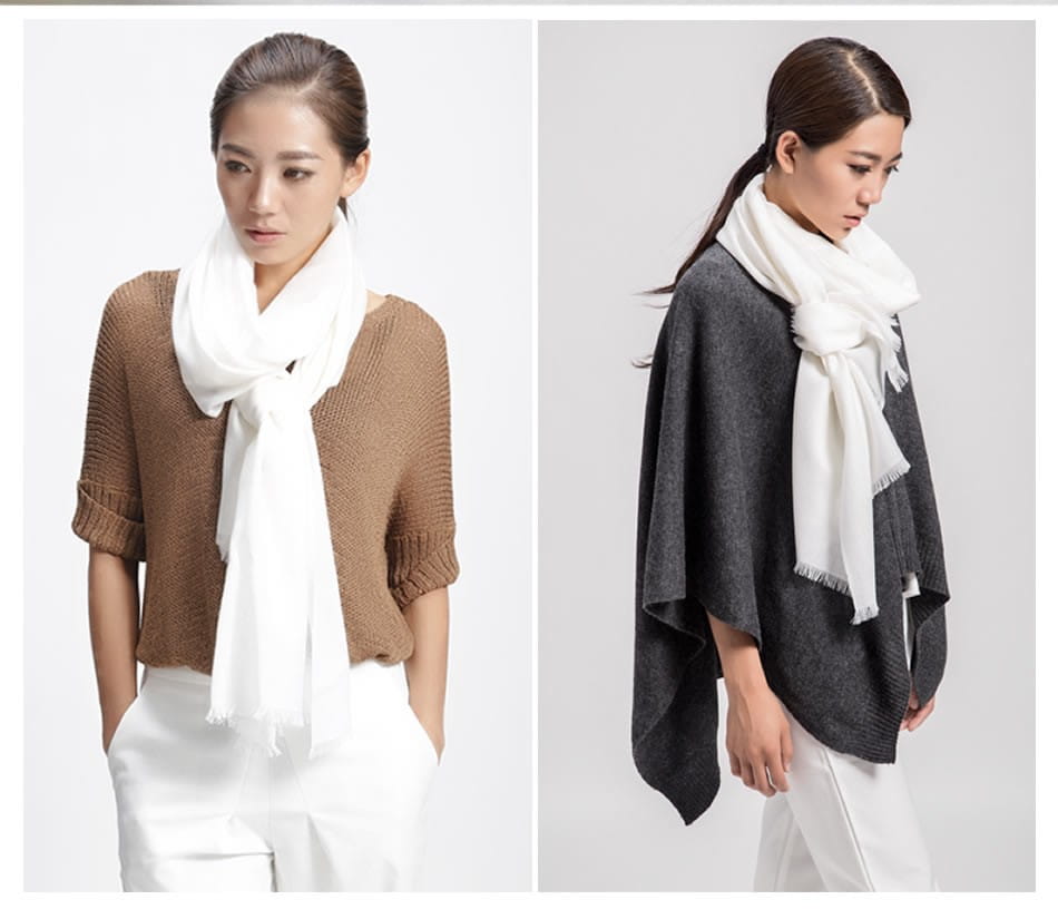 Bufanda de lana de lujo para mujer en color blanco, con bordes deshilachados, llevada sobre una parte superior de punto marrón y combinada con pantalones blancos.
