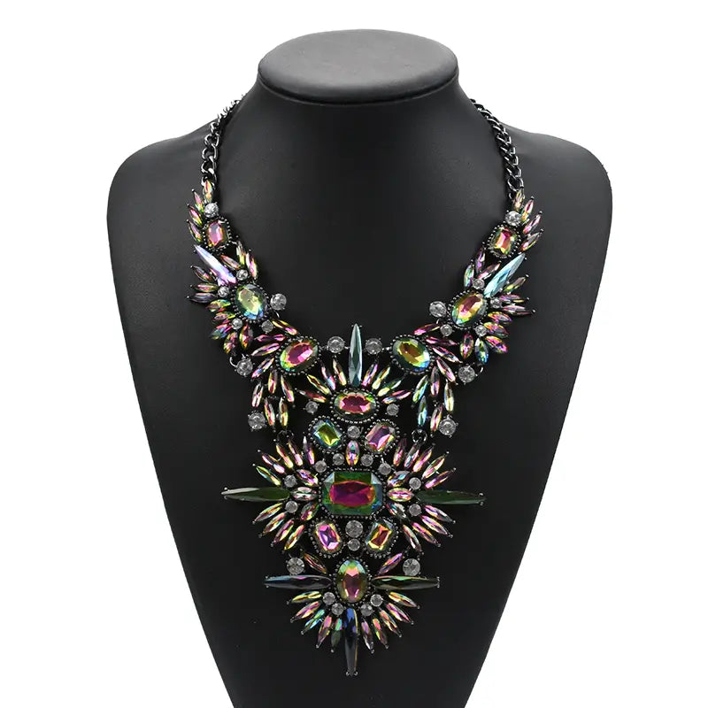 Un collier d’affirmation en cristal irisé audacieux, avec une cascade de pierres précieuses multicolores et des accents métalliques sur une chaîne noire, conçu comme un ras-du-cou bohème.