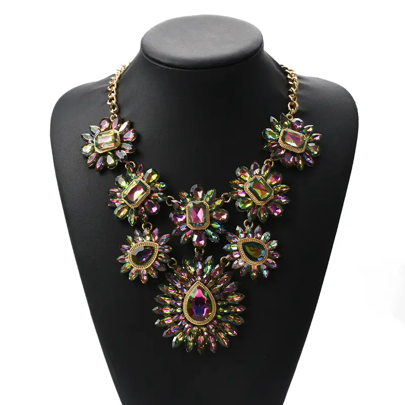 Un collier d’affirmation en cristal bohème multicolore vibrant, au design superposé, avec des pierres précieuses irisées rose et vert serties dans une monture en métal à tons dorés.