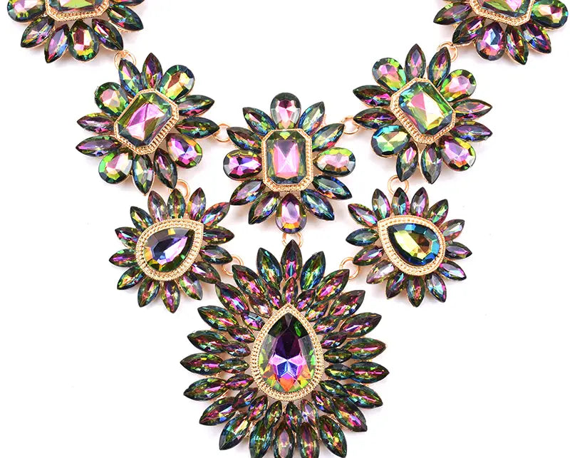 Un collier d’affirmation en cristal irisé vibrant, avec une pierre centrale en forme de goutte, entourée de pétales en cristal multicolores irisés disposés dans une monture en métal à tons dorés, dans un style multicolore de ras-du-cou bohème.