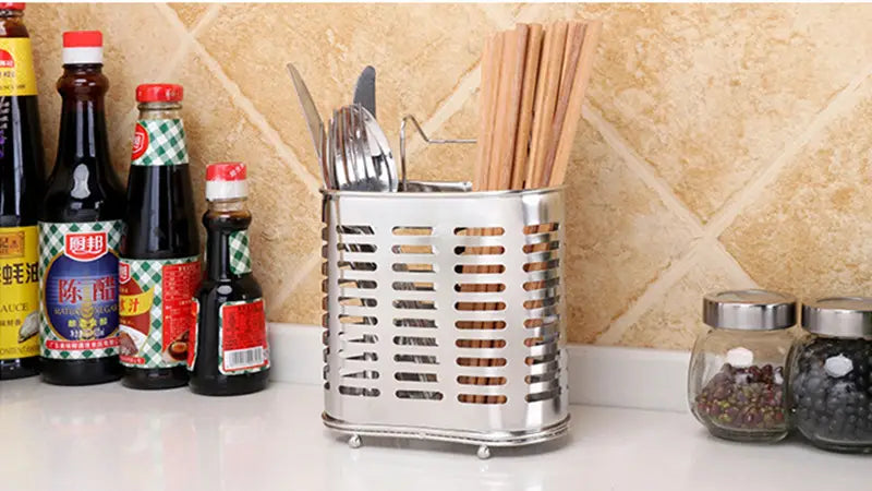 Silver stainless steel cutlery and utensil storage rack with a perforated design and small feet holding chopsticks and cutlery.